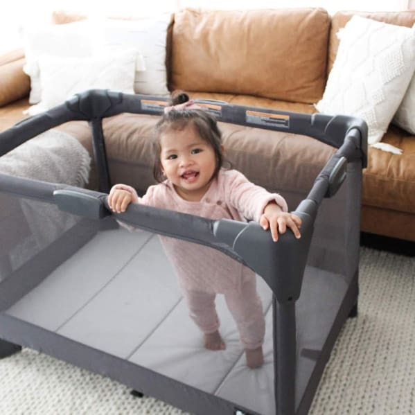 A baby in a playpen with pillows on the couch