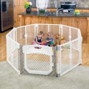 A baby playing in the corner of a room with a play yard.