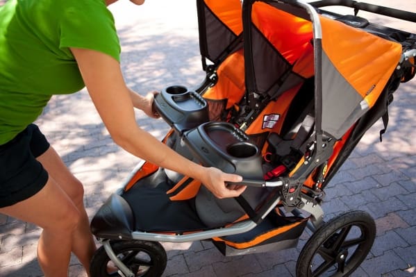 A person pushing an orange stroller with the handle bar extended.